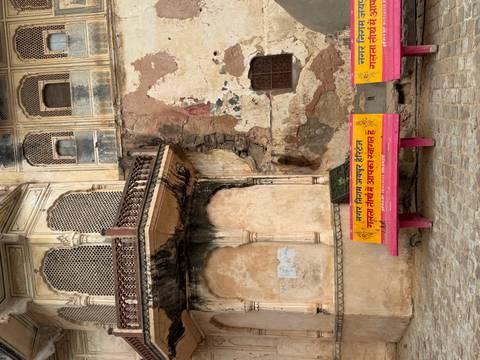Weather-worn heritage building façade with ornate balconies and bright Hindi welcome benches in front.