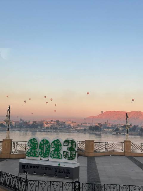 Dozens of hot-air balloons drift over Luxor’s west bank at dawn, tinting the sky pink above quiet waters.