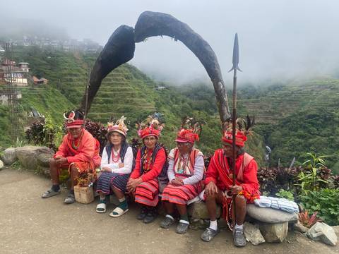 Group of indigenous elders in traditional attire seated before misty rice terraces