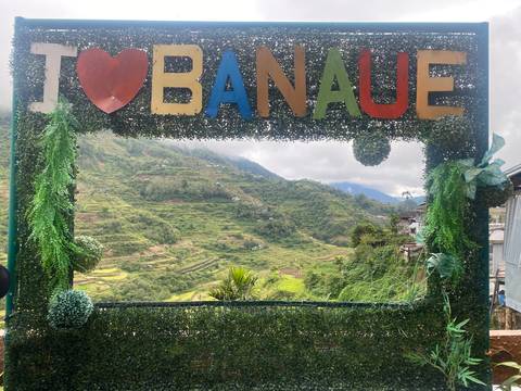 Decorative frame covered in greenery spelling out “I ♥ Banaue” overlooks tiered rice terraces and lush mountains.