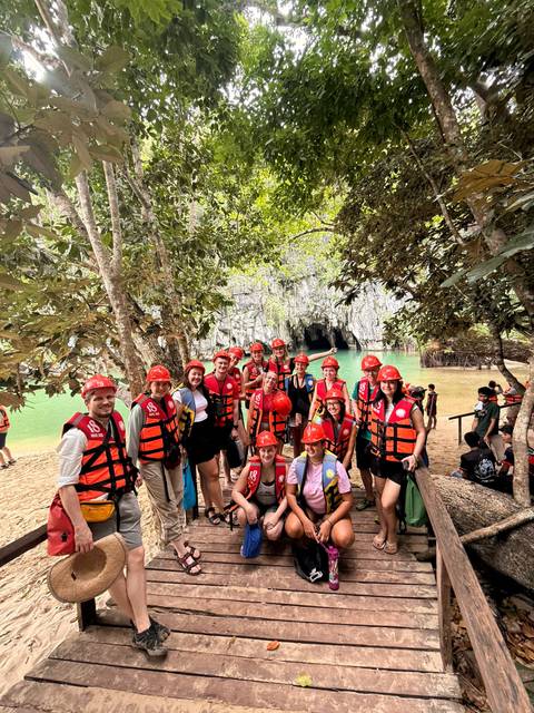 Tour group in life vests and helmets pose before Puerto Princesa Underground River entrance.