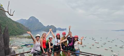 Friends in climbing gear raise arms atop viewpoint overlooking El Nido’s karst bay.