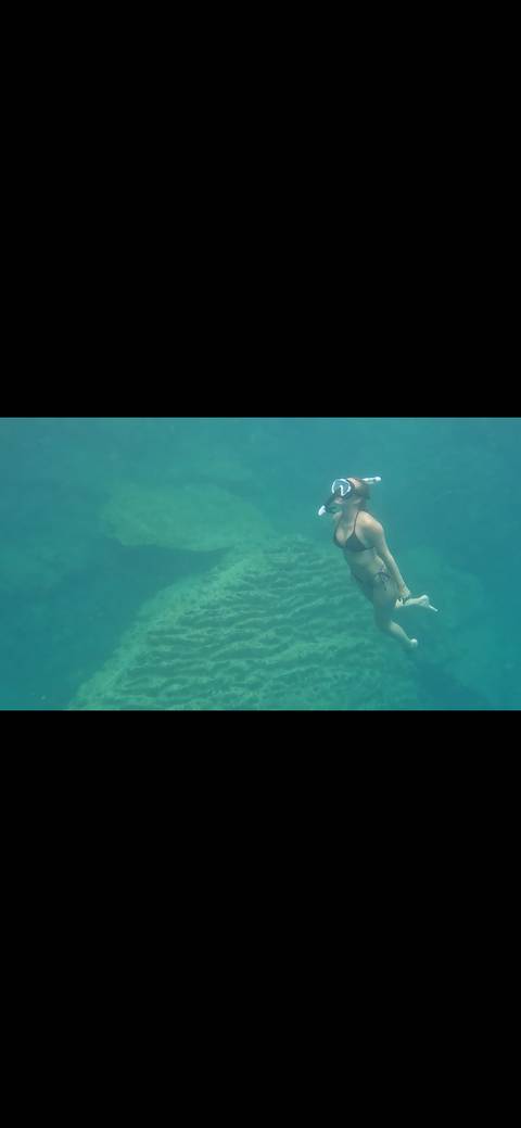 Underwater shot of snorkeler gliding above coral rock in clear blue sea.