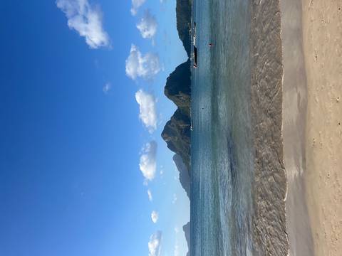 Serene tropical beach with clear water and dramatic limestone islands under blue sky.