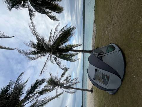 Small grey tent pitched beneath swaying palm trees beside a tranquil tropical lagoon.