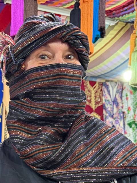 Close-up portrait of a woman wearing a colourful striped headscarf and face covering in a market stall.