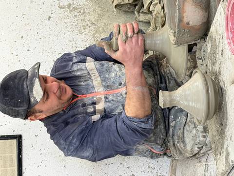 Artisan potter shapes a clay tagine on a wheel, covered in grey splatters of wet clay.