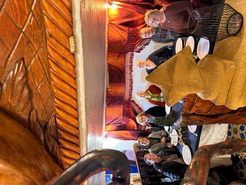 Group seated for a meal inside a low-ceilinged room decorated with tapestry fabrics.