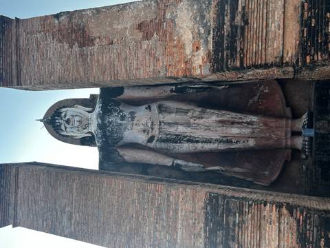 Tall standing Buddha statue weathered with age between brick walls in Sukhothai.