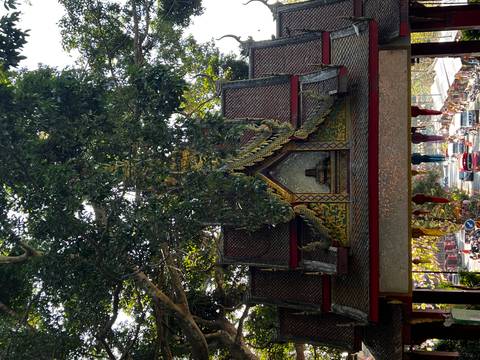 Decorative Thai temple entrance framed by lush trees overlooking a busy street below.