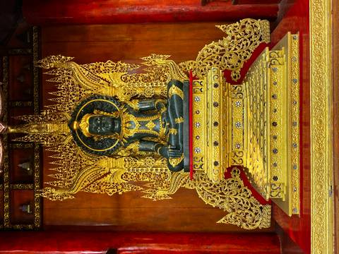 Ornate dark-green Buddha statue sits on an intricately gilded throne inside a Thai temple.