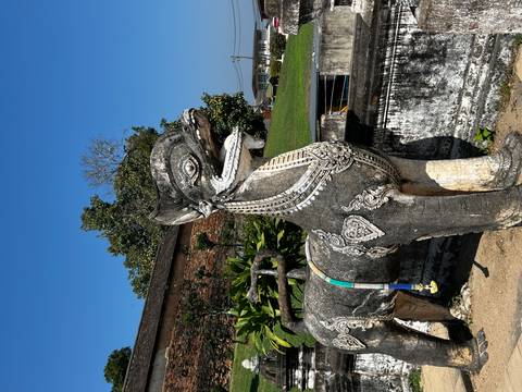 Ornate stone guardian lion statue stands outside a Thai temple on a sunny day.