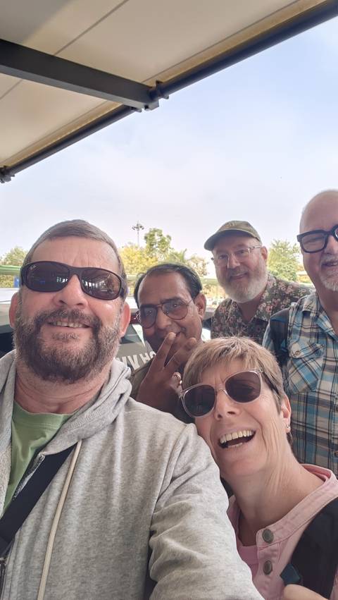 Close-up selfie of five travellers smiling outside a vehicle with trees in background.