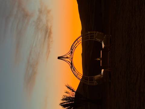 Artistic circular metal pavilion silhouetted against an orange desert sunset.