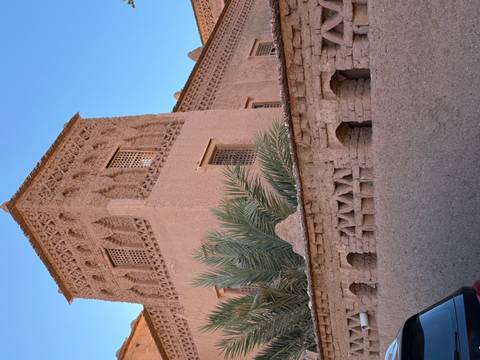 Adobe kasbah tower with ornate Berber designs and palm fronds against a clear sky.