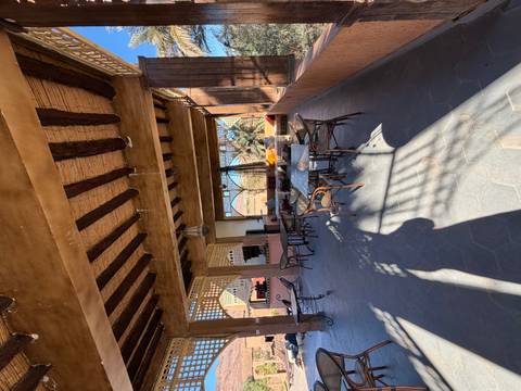 Shaded open-air lounge with rustic wooden beams, mosaic tables and desert views beyond.