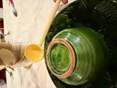 Close-up of an upside-down green ceramic bowl on a patterned platter with a wooden ladle beside it.