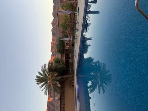 Still swimming pool reflecting a palm tree and sun-tinted mountains at dawn in a desert lodge courtyard.