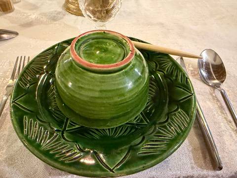 Top-down shot of a green glazed bowl set on an ornate leaf-pattern platter with cutlery and wooden spoon.