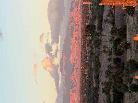 Sun-kissed mountain range above a patchwork of palm groves and scattered buildings in the early evening light.