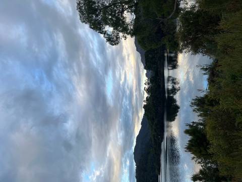 Still lake at dusk reflecting silhouetted treeline and brooding evening clouds.