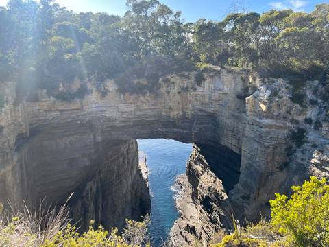 Sunlit natural sea arch reveals sparkling blue water through its cavernous opening.