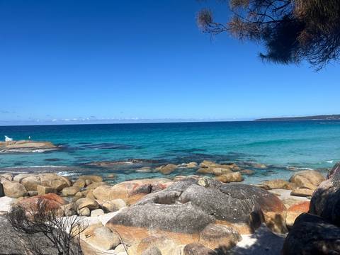 Crystal-clear turquoise sea laps against rounded granite boulders under a cloudless sky.