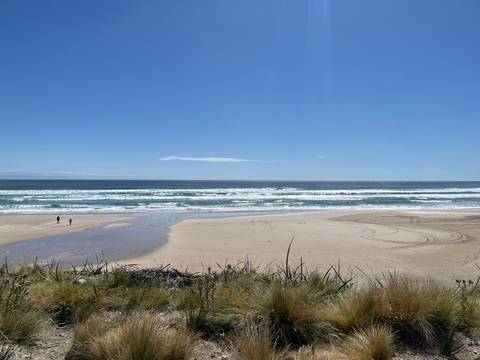Wide sandy beach with two distant walkers beside rolling surf.