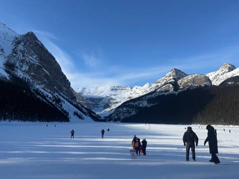 Visitors walk and skate across the frozen expanse of Lake Louise surrounded by snow-capped peaks.