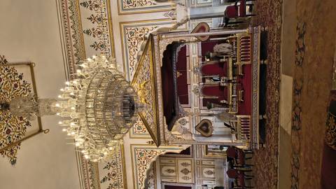 Opulent throne room with huge chandelier, ornate canopy and regal chairs.