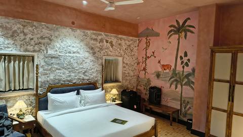 Stylish hotel room with stone accent wall, painted mural and neatly made bed.
