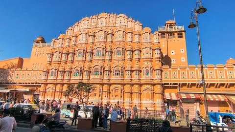 Iconic orange facade of Hawa Mahal bathed in bright morning light with bustling street below.