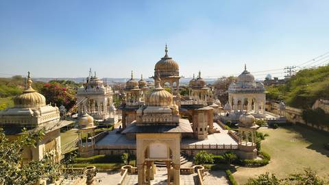 Ornate cenotaph complex with golden domes and manicured gardens under clear sky.