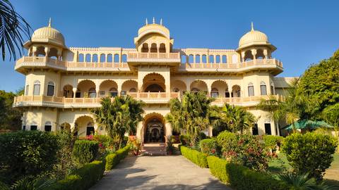 Heritage palace hotel with yellow domes, arched balconies and lush gardens.