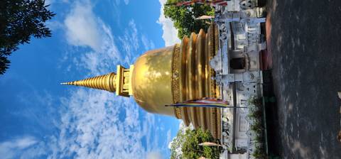 Brilliant gold stupa with a pointed spire under vivid blue skies and fluttering prayer flags.