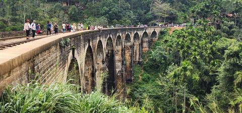 Tourists walk along the famous Nine Arches railway bridge spanning a lush green valley.
