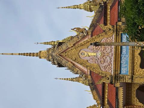Close-up of an ornate golden pagoda roof and spire of a Buddhist temple with intricate carvings and Khmer script sign.