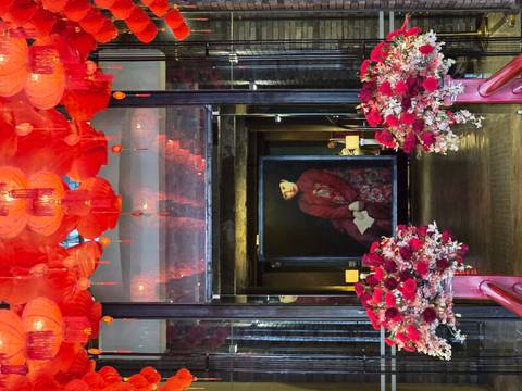 Elegant interior decorated with red lanterns and floral arrangements framing a portrait painting behind glass doors.