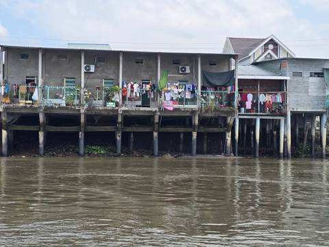 Stilt houses with laundry hanging over muddy river water in a riverside community.