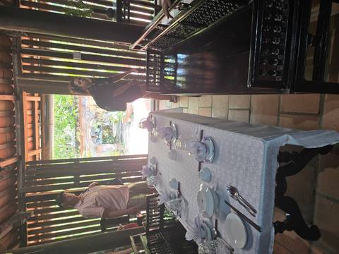 Two travellers standing beside a set dining table inside a rustic house with open wooden doors to a garden.