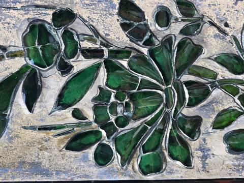 Close-up of stained-glass mosaic depicting green floral and bamboo motifs in earthy tones.