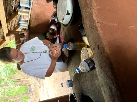 Young traveller preparing food by hand in a rustic open-air kitchen with simple utensils and plastic water bottles.