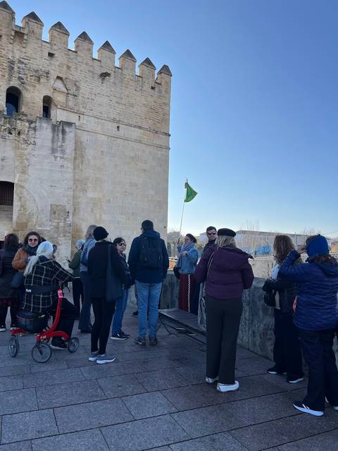 Tour group gathered outside a historic stone tower with a green flag fluttering on a sunny morning.