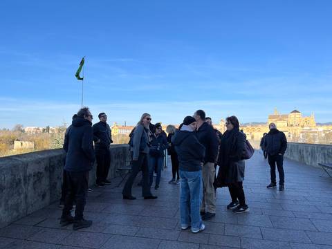 Tour group standing on a stone bridge overlooking Cordoba with the Mezquita cathedral visible in the distance.