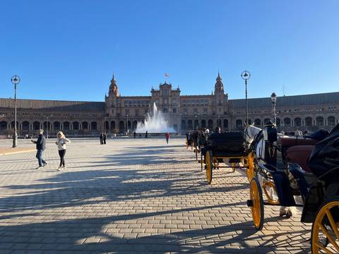Wide view of Seville's Plaza de España with its grand Renaissance-style building, central fountain and horse carriages.