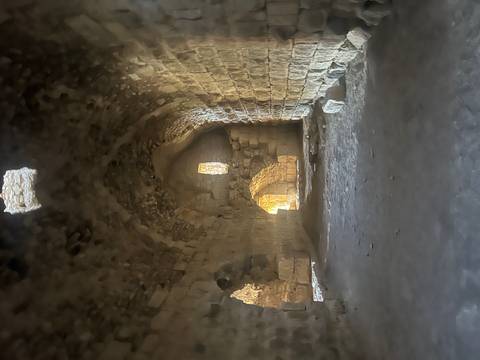 Stone-arched interior passage of an ancient ruin lit by soft natural light through small windows.