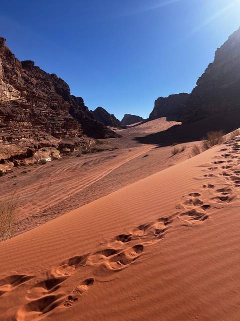Rippling sand dunes and rocky cliffs of Wadi Rum marked with fresh footprints.