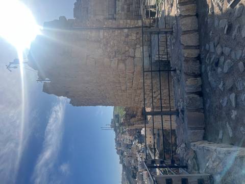 Sun flare peeks over the stone walls of a hilltop Jordanian fortress overlooking a town below.