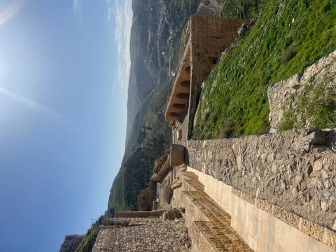 Ancient stone fortress walls overlook rolling green valleys under a bright sky.