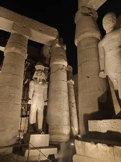 Night-lit colossal columns and Pharaoh statue inside Luxor Temple complex.